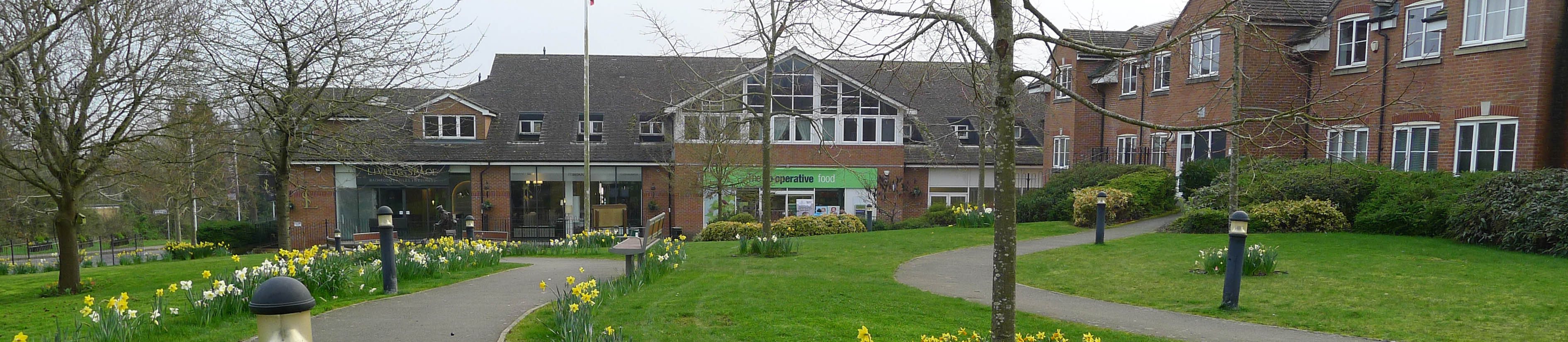 Shops at Bells Hill Green, with grassed area and daffodils in the foreground
