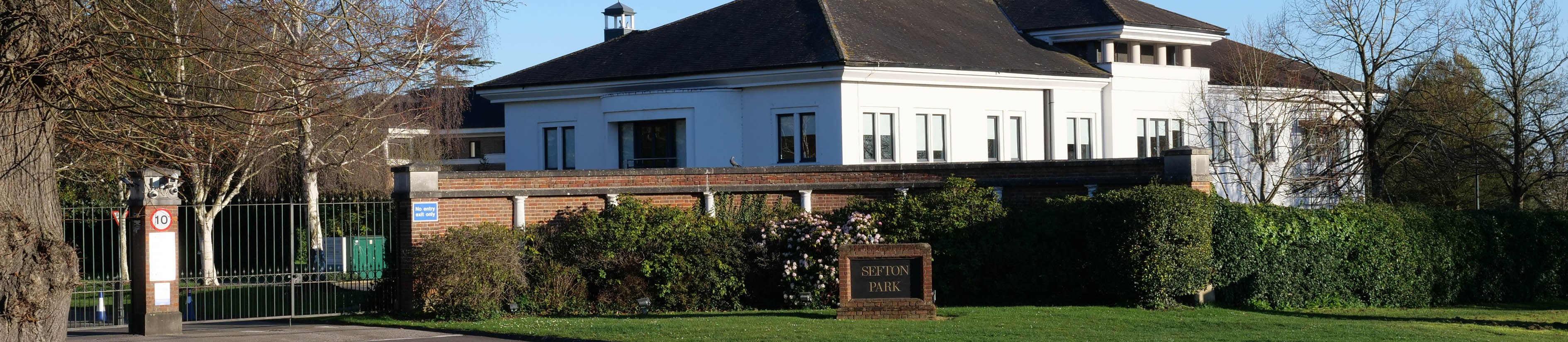 A large, white office building sits beyond a brick wall at Sefton Park on Bells Hill in Stoke Poges